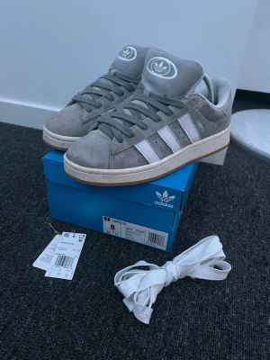 Adidas Campus 00S Grey - Plagg:Adidas Campus 00s Storlek:41 1/3 Nypris:1399 Mitt pris:599 Skick:9/10 Märke/Brand:Adidas Färg:Grå/Vit Material:Mocka Passform:41-42 även 43 Stora i Storleken Användning:Sparsamt använda Övrigt:  Kvitto finns på Mail, Kan maila de vid köp😃  Priset är inte hugget i sten🪨🪓 Fraktar Inom 24 h📦 Skriv Vid Minsta Lilla Intresse😃