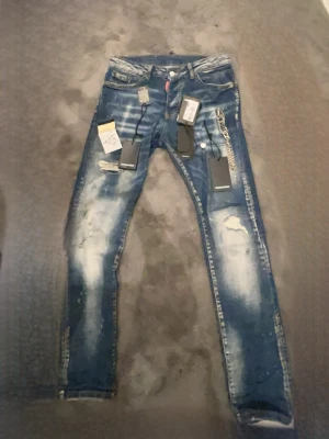 Blå skinny jeans från Dsquared2 - Säljer ett par blå skinny jeans från Dsquared2 med slitningar, tvättade detaljer och kedja i midjan. Jeansen har klassisk femficksmodell, låg midja och är tillverkade i bomull med stretch. Perfekta för dig som vill ha en edgy och trendig look.