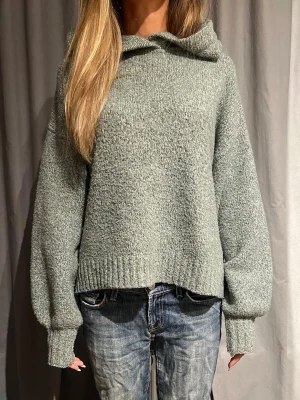 Stickad hoodie med luva - Mysig stickad hoodie med luva och breda, långa ärmar. Tröjan har ribbade muddar vid ärmslut och nederkant samt en avslappnad, loose passform. Perfekt för dig som gillar en chill och enkel stil. Mysig och skön hoodie, sticks inte. 