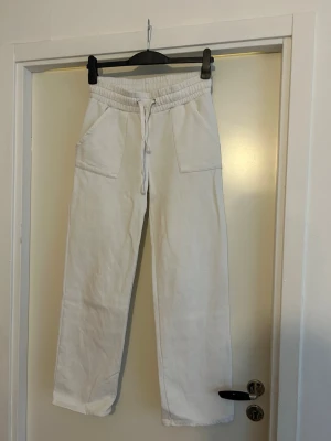 Vita mjukisbyxor med snörning - Säljer ett par vita mjukisbyxor med bred resår i midjan och snörning framtill. Byxorna har två stora fickor fram och två bakfickor. De är raka i modellen och gjorda i mjukt bomullstyg. Perfekta för chill dagar eller när du vill vara extra bekväm.