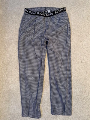 Rutiga pyjamasbyxor från Björn Borg - Snygga pyjamasbyxor från Björn Borg med svart resår i midjan och logotyp. Byxorna har ett blått och vitt rutmönster och är tillverkade i ett mjukt och bekvämt tyg, perfekta för att chilla hemma. Ganska korta i storleken, mer en 164 än 170.
