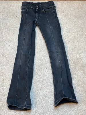 Svarta bootcut jeans med vita sömmar - Snygga svarta jeans med vita kontrastsömmar och bootcut passform. Klassisk femficksmodell med dubbla knappar i midjan och raka ben som släpper ut vid ankeln. Perfekta för dig som gillar en retrovibe och vill ha något som sticker ut.