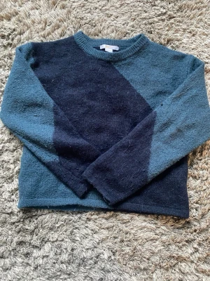 Blå stickad tröja med diagonal detalj - Mysig stickad tröja i två nyanser av blått med en diagonal mörkblå panel framtill och baktill. Tröjan har rund halsringning och långa ärmar. Perfekt för dig som gillar en enkel men ändå unik look. Storlek 146/152💕