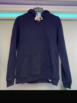 Les deux hoodie  - Mörkblå hoodie från les deux med stor känguruficka framtill och vita dragsnören i huvan med färgade ändar. Hoodien har ribbade muddar vid ärmslut och nederkant. Perfekt för en avslappnad och stilren look. Ny pris 1100kr mitt pris 150kr