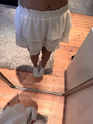 Vit volangkjol med resårmidja från Chelsea - Söt vit kortkjol med dubbla volanger och bred resår i midjan. Kjolen har en luftig och flowy känsla, perfekt för varma dagar. Tillverkad i ett lätt material som ger en skön passform och snygg siluett.