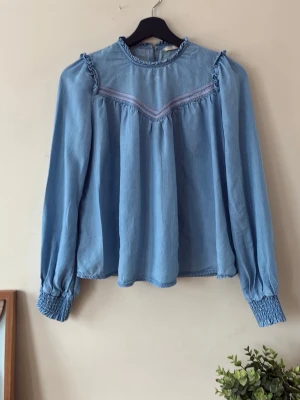 Elegant blus från Esprit - Säljer en blå blus från Esprit i storlek XS. Använd bara 2 ggr och är i  mycket fint skick. Elegant modell med volangdetaljer vid halsringning och axlar samt långa ärmar med smockade muddar. Perfekt både till vardag och fest!