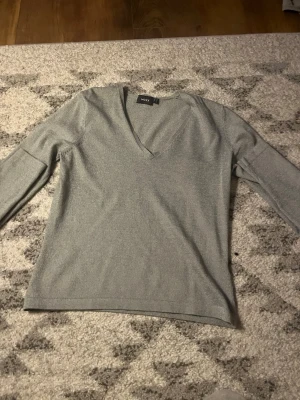 Ljusgrå V-ringad tröja från Moxx - Snygg ljusgrå tröja från Moxx med V-ringning och långa ärmar. Enkel och stilren design som passar perfekt till jeans eller kjol. Mjuk och skön känsla, perfekt för lager-på-lager-stil.