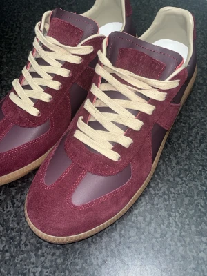 Ett par sneakers från Maison Margiela - Ett par sköna Gats sneakers i vinröda sneakers med beige snörning och detaljer i mocka och syntet. Skorna är i nyskick, 9/10, perfekt för en trendig och avslappnad look, och priset är satt därför då kvitto o box saknas. Hör gärna av dig om du undrar över något!!! !!‼️