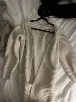 Beige stickad kofta från H&M - Mysig beige stickad kofta från H&M med öppen front och två stora fickor framtill. Koftan har lång ärm och ribbad struktur, perfekt att slänga på sig över en t-shirt eller topp. Enkel och stilren design som passar till det mesta.