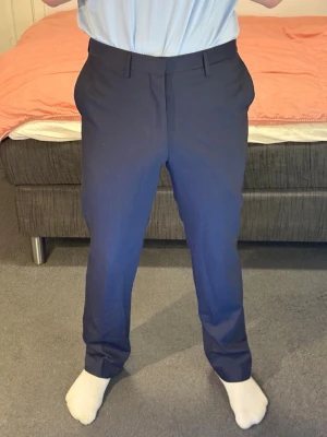 Mörkblå kostymbyxor herr - Snygga mörkblå kostymbyxor med klassisk rak passform och pressveck. Byxorna har bälteshällor, två sidofickor fram och två bakfickor med knapp. Perfekta för en stilren och uppklädd look.