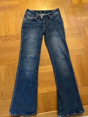 Blå bootcut jeans med broderade fickor - Säljer ett par klassiska blå lowwaist bootcut jeans med snygga broderade detaljer på bakfickorna. Säljer dessa jeans eftersom storleken inte passat. Obs: lite slitet vid nederkanten av byxorna. Kontakta gärna om du är intresserad! 💕