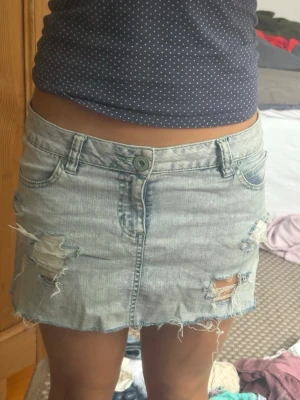 Ljusblå jeanskjol med slitningar - Säljer en ljusblå kort jeanskjol med slitna detaljer och fransig nederkant. Kjolen har klassiska fem fickor, bälteshällor och knappstängning framtill. Perfekt för dig som gillar en avslappnad och trendig stil. Från only