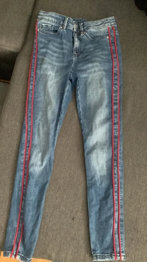 Blå jeans med röda ränder - Blå jeans med två röda ränder längs båda benen. Midrise. Slim. W26, L32