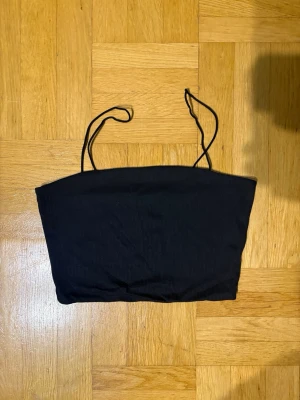 Svart ribbad linnetopp - Snygg svart ribbad linnetopp med tunna axelband. Perfekt att styla med jeans eller kjol för en clean och enkel look. Toppen är croppad och har en smickrande passform.