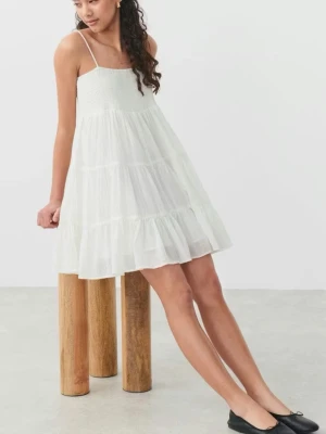 Vit somrig kortklänning med volanger - Söt vit kortklänning med tunna axelband och volangdetaljer. Klänningen har en luftig passform och är perfekt för varma dagar. Tillverkad i lätt bomullsmaterial som känns skönt mot huden. Enkel och stilren design som ger en fräsch look.