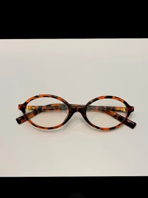 Oanvända bruna ovala blåljusglasögon i sköldpaddsmönster  - Snygga solglasögon med oval form och sköldpaddsmönstrad. Bågarna är tunna och lätta, perfekta för en trendig look. Materialet är plast och designen är klassisk men ändå modern.
