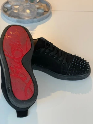 Christian Louboutin skor - Säljer ett par svarta sneakers från Christian Louboutin i mocka med ikonisk röd sula och svarta nitar på tån. Skorna har snörning och en rund tå. Dom är i helt okej skick tre nitar på den vänstra skon är av men man märker inte av det så mycket. Inuti skon har typ all färg o text försvunnit men inte något man ser när man har på sig dom och dom är lite repade på undersidan, också lite gått sönder på kanten uppe. Vet ej om de är äkta men tror de är det för ja köpte dom begagnat. Pris går diskutera👍