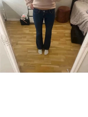Blå bootcut jeans med låg midja - Säljer ett par blå bootcut jeans med låg midja. Jeansen har klassisk femficksdesign och är tillverkade i ett mjukt denimtyg som sitter snyggt över höfterna och släpper ut vid benen. Perfekta för en trendig och avslappnad look.