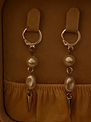 Silvriga örhängen med pärlor och spikes - Säljer ett par trendiga örhängen i silverfärg med två vita pärlor och en spetsig metallspets längst ner. Örhängena har en cool kombination av klassiska pärlor och edgy detaljer. Perfekta för dig som vill sticka ut lite extra.