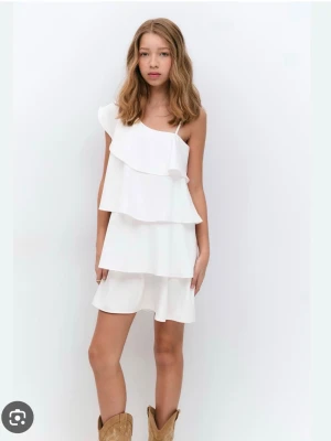 Vit volangklänning med axelbandslös design - Säljer nu min konfa/sommar klänning. Snygg vit kortklänning med flera volanger och smala axelband. Klänningen har en luftig passform och är perfekt för varma dagar. Enkel och stilren design som känns fräsch och modern. Hör av er för fler bilder 