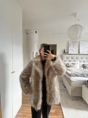 Beige fluffig pälsjacka - Säljer en oversized beige pälsjacka med fluffig känsla och bred krage. Jackan har en naturlig färgskiftning i beige och brunt och är perfekt för kalla vinterdagar. Stängs framtill och har en klassisk rak passform. Från märket Reserved