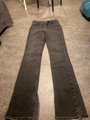 Mörk gråa raka jeans med skarp kant - Säljer ett par mörkgråa jeans med rak passform och råa, fransiga benslut. Jeansen har klassisk femficksdesign och knappgylf. Perfekta för en avslappnad och trendig look. Säljer dessa jeans då jag inte tycker att de passar mig lika fint😊