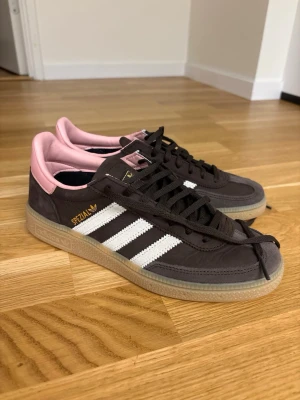 Adidas Spezial bruna sneakers storlek 38,5 - Helt nya snygga Adidas Spezial sneakers i brunt mocka med vita klassiska ränder på sidan och rosa detaljer vid hälen. Gummisula och svart snörning ger en retro vibe. Perfekta för dig som vill ha en unik touch på din streetwear.
