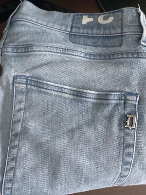 Ljusblå/grå dondup jeans - Säljer ett par ljusblå super skinny jeans från Dondup Jeansen har klassisk femficksdesign, en snygg metall-logga på bakfickan och är tillverkade i ett mjukt denimtyg. Perfekta för dig som gillar en tight passform och stilren look. Modell Roddy super skinny fit med slitningar. Passar dig mellan 165-175. 
