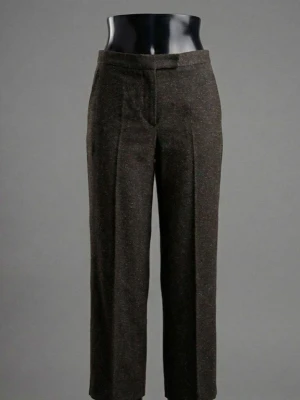 Mörkbruna kostymbyxor med prickar - Snygga mörkbruna kostymbyxor med diskreta orangea prickar. Byxorna har hög midja, raka ben och klassisk knappstängning fram. Materialet känns mjukt och har en lätt struktur, perfekt för dig som gillar en stilren look med lite edge.