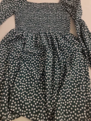 Grön blommig kortklänning - Supersöt grön klänning med vita blommor och smockad överdel. Klänningen har långa ärmar med lätt puff och är perfekt för dig som gillar en feminin och trendig stil. Den har en kort längd och ett flowigt fall i kjolen.