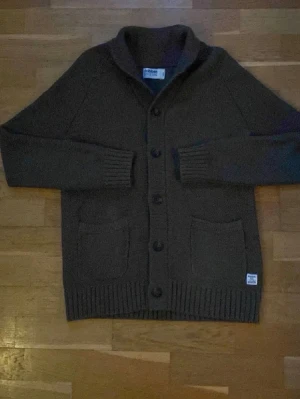 Mörkgrön kofta från Dobber - Säljer en mysig mörkgrön stickad kofta från Dobber med sjalkrage och knäppning framtill. Två stora fickor framtill och ribbade muddar vid ärmslut och nederkant. Perfekt för lager-på-lager och chill stil.