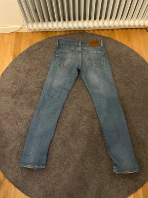 Blå skinny jeans från Levi's - Säljer ett par klassiska blå skinny jeans från Levi's med fem fickor och snygga slitningar på framsidan. Jeansen har en ljus tvätt och är tillverkade i bomull med lite stretch för extra komfort. Perfekta för en avslappnad och trendig look.