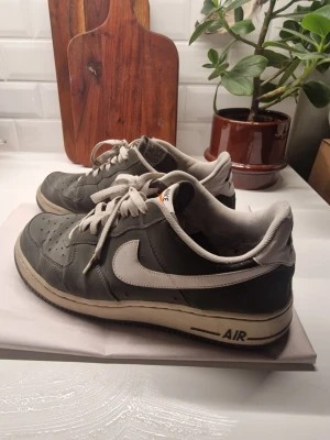  GRÖNA NIKE AIR FORCE 1  - Klassiska Nike Air Force 1 sneakers i grönt skinn med vita detaljer och snörning. Modellen har en vit sula med svart AIR-tryck och den ikoniska swoosh-loggan på sidan. Perfekta för dig som gillar streetwear och tidlös stil. Den ena skon är lite sliten på insidan av hälen.