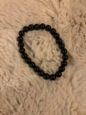 Svart pärlarmband i elastisk modell - Snyggt armband med svarta, runda pärlor trädda på en elastisk tråd. Perfekt accessoar för att ge din outfit en stilren touch. Passar både ensam eller i kombination med andra armband.