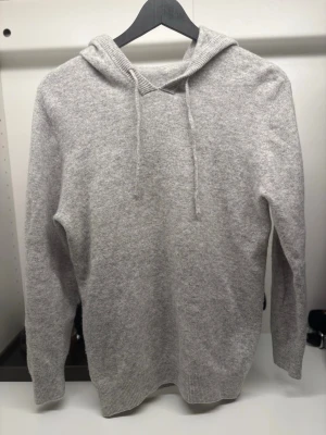Ljusgrå stickad hoodie med huva - Mysig ljusgrå stickad hoodie med huva och dragsnören. Tröjan har långa ärmar och ribbade muddar vid ärmslut och nederkant. Perfekt för en avslappnad och stilren look. Materialet känns mjukt och skönt mot huden. Super bra skick, super snygg, har du några frågor så fråga gärna, svarar snabbt🙌🔥💸