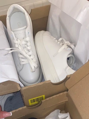 Vita sneakers från Calvin Klein - Stilrena vita sneakers från Calvin Klein med klassisk låg profil och tjock sula. Skorna har vita snören, diskret logga på plösen och är tillverkade i slätt läderliknande material. Perfekta för en clean och modern look.