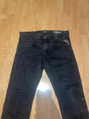 Svarta jeans från Replay - Säljer ett par svarta jeans från Replay med klassisk femficksdesign och raka ben. Jeansen har snygga detaljer på bakfickorna och en patch med Replay-logo baktill i midjan. Tillverkade i bomull med en lätt tvättad look.