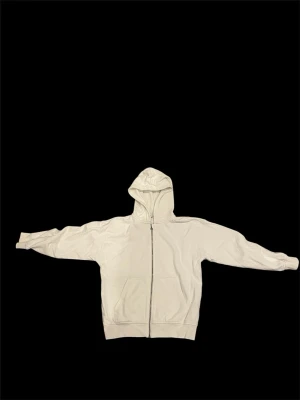 Vit zip hoodie med luva - En stilren vit hoodie med dragkedja framtill och stor huva. Hoodien har två fickor på magen och ribbade muddar vid ärmslut och nederkant. Perfekt för en avslappnad och trendig look. Materialet känns mjukt och bekvämt.