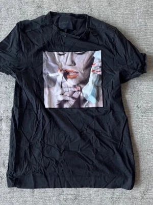 Svart t-shirt med grafiskt tryck Limtato - En lite schysstare svart tischa från Limtato med soft tryck. T-shirten har rund halsringning och korta ärmar. Perfekt för dig som gillar unika statement-plagg. Passar under en kavaj, Kashmir tröja eller bara som den är. Den är i fint skick. Hör av er vid frågor och funderingar! 