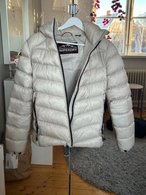 Beige dunjacka från Superdry - Snygg beige dunjacka från Superdry med huva och svarta dragkedjor