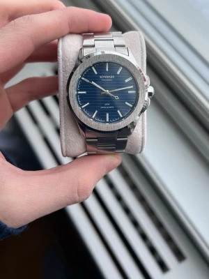 KOMPASS silverfärgad armbandsklocka - Stilren armbandsklocka från KOMPASS med blå urtavla och silverfärgat armband i rostfritt stål. Klockan har minimalistiska index, datumvisning och klassisk rund form. Drivs av japanskt kvartsurverk och har en polerad finish som ger en modern look. Batteriet behövs bytas men annars är den i topp skick!