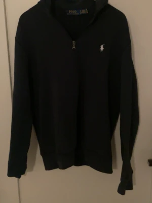 Marinblå half zip tröja Polo Ralph Lauren - Orginellt pris på tröjan är 2100 ,Snygg marinblå långärmad tröja från Polo Ralph Lauren med half zip och ståkrage. Tröjan har det klassiska broderade Polo-logot på bröstet och är gjord i mjuk bomull. Perfekt för dig som gillar stilren och sportig look. Liten flöck som enkelt försvinner i tvätten funkar som liten medium också