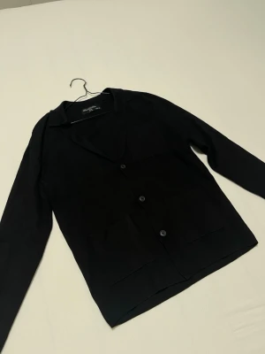 Daniel de prati stickad kofta/kavaj - Stilren svart kofta/kavaj från Daniel de prato med tre knappar framtill och två stora fickor. Klassisk krage och rak passform. Perfekt för lager på lager och enkel att matcha med olika outfits. Den är oanvänd och jag säljer den eftersom den inte passar mig.