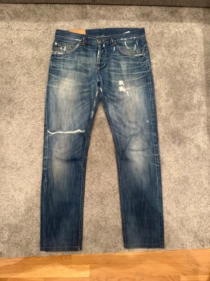 Dondup jeans  - Säljer ett par blå dondup jeans med snygga slitningar som är mycket eftertraktade just nu. Jeansen är i storlek W33 och 9/10 skick ✅ 