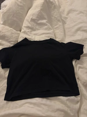 Svart croppad t-shirt från 157 - En svart croppad t-shirt från 157 i mjuk bomull. Enkel och stilren design med rund halsringning och korta ärmar. Perfekt att matcha med jeans eller kjol för en avslappnad look.