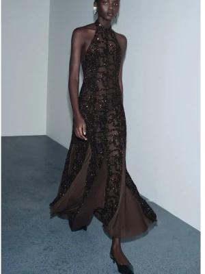 Brun glittrig långklänning med halterneck  - Elegant brun långklänning med halterneck och glittriga paljettdetaljer. Klänningen har en figurnära passform upptill och vidd nertill, vilket ger en snygg siluett. Perfekt för speciella tillfällen när du vill sticka ut.
