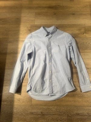Polo Ralph Lauren skjorta - Klassisk ljusblå skjorta från Polo Ralph Lauren med button-down krage och broderad logga på bröstet. Skjortan har långa ärmar, knappar framtill och är tillverkad i mjuk bomull. Perfekt till både jeans och chinos.