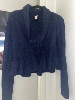 Mörkblå stickad kofta med volang - Mysig mörkblå stickad kofta med volangkant och knytband framtill. Koftan har lång ärm och en bred krage. Materialet känns mjukt och stretchigt. Storlek XS, pris kan diskuteras!💕💕 