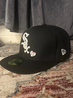 Svart White Sox keps från New Era - Säljer en svart keps från New Era med White Sox-logga broderad i vitt framtill och ett litet baseballemblem. På sidan finns ett broderat 'World Series 05'-märke. Klassisk 59Fifty-modell med rak skärm och broderad New Era-logga på sidan.