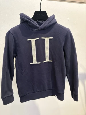 Les Deux Mörkblå hoodie  - Mörkblå hoodie med stor vit II-logga framtill. Klassisk modell med huva och ribbade muddar vid ärmslut och nederkant. Perfekt för en avslappnad och cool stil.